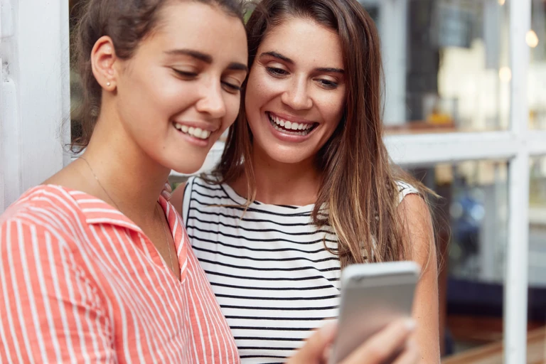 Two smiling women looking at a phone together